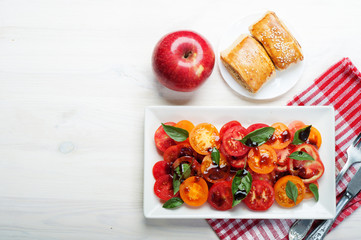Light dietary salad with organic tomatoes, balsamic vinegar, olive oil, salt and basil leaves in a...