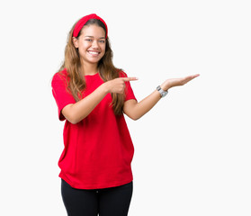 Obraz na płótnie Canvas Young beautiful brunette woman wearing red t-shirt over isolated background amazed and smiling to the camera while presenting with hand and pointing with finger.