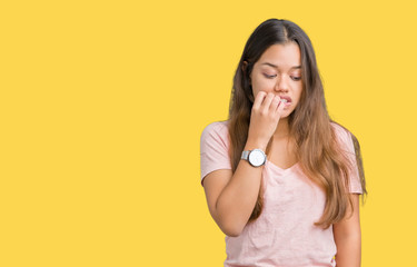 Young beautiful brunette woman wearing pink t-shirt over isolated background looking stressed and nervous with hands on mouth biting nails. Anxiety problem.