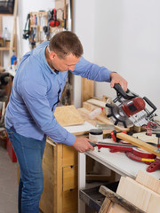 Woodworker male  cutting wooden plank with fret saw in workplace