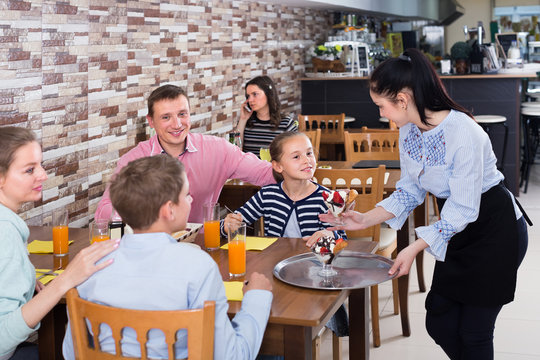 Polite positive waitress bringing ordered dishes to family