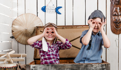 two little kids in pilot hats in big old chest making glasses with hands