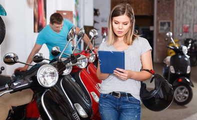 Smiling female is shopping and choosing new motobike in moto store.