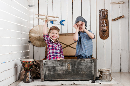 smiling little girl with wooden plane in hand and boy in pilot hat sitting in big chest