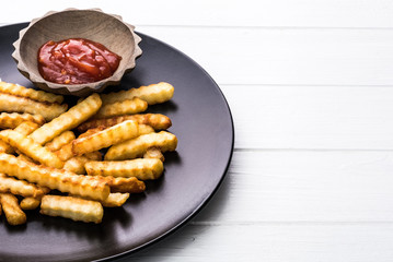 French potatoes with bowl of ketchup on black plate, white background.