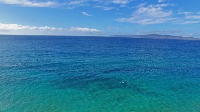 Panning aerial shot of a Snorkler in Maui Hawaii in beautiful blue water with sandy beach and land in background
