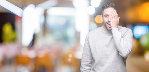 Obraz premium Young handsome man wearing sweatshirt over isolated background covering one eye with hand with confident smile on face and surprise emotion.