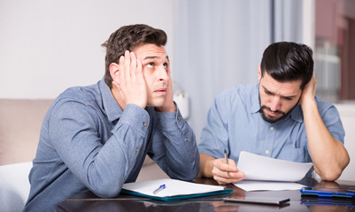 Two troubled men reading documents at desk