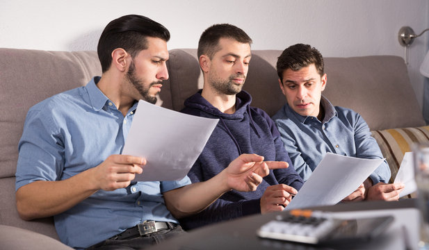 Three serious males discussing documents on couch