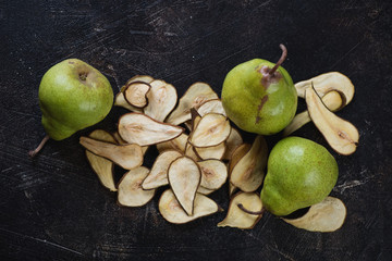 Pear fruit chips and fresh pears on a dark brown stone background, high angle view, horizontal shot