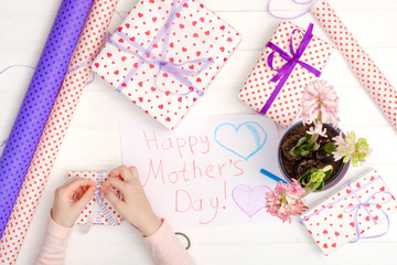 Little girl drawing happy mother's day greeting card with presents on the table. Mothers day background