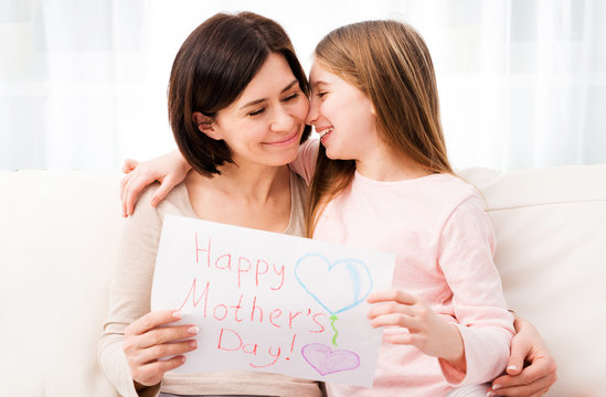 Lovely little girl hugging her mother , Girl holding creative handmade greeting card for mother. Daughter congratulates mom and gives her postcard for Happy Mother's day