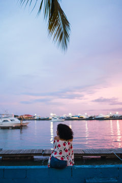 Woman sitting on seafront in colorful sunset time