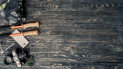 Preparation for journey. Hiking boots, trekking pole, camera, lenses and mobile phone on vintage wooden background. Tourist lifestyle concept