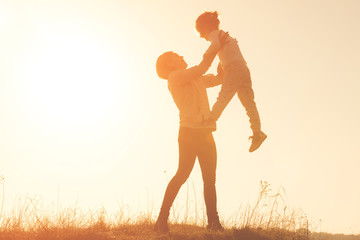 Silhouette of smilling young mother throwing up baby in the sky at sunset. Mother with child girl playing together in the field