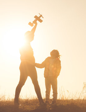 Silhouette of mother and daughter playing in the field with small airplane toy against vivid orange sky. Happy mother and daughter at sunset time