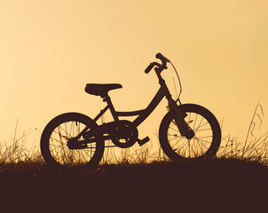 Fototapeta premium Child's bike silhouette at the sunset on the countryside. Dark silhouette of bicycle