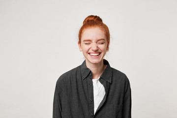 Cheerful resilient red-haired girl with a bun at her head laughs sincerely, having closed her eyes,...