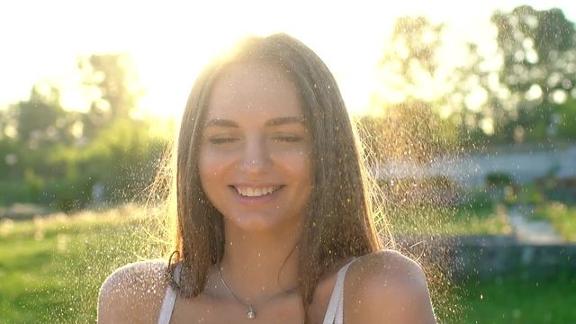 Fashion model girl in golden sparkles glitter posing. Portrait of beautiful woman with glitter confetti outdoors. Caucasian teenage glowing gold skin shine make-up in summer at sunset. Outside Beauty