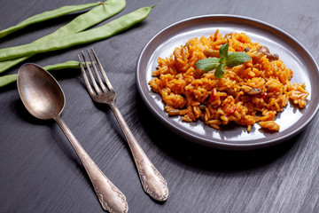 Paella of vegetables and chicken on black table, spoon, fork and beans.