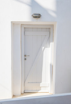 Front view of white wooden door in a whitewashed wall. Traditional facade of Greek house
