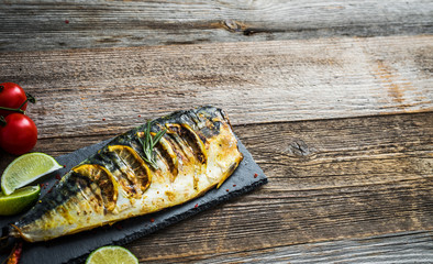 Fried mackerel fillets with lime on black slate board, wooden background