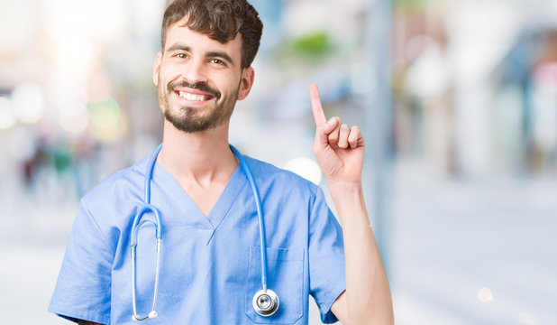 Young handsome nurse man wearing surgeon uniform over isolated background showing and pointing up with finger number one while smiling confident and happy.