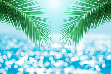 Fototapeta na wymiar Blur Sea water bokeh against sunlight background with palm leaf on foreground. Free space for text.