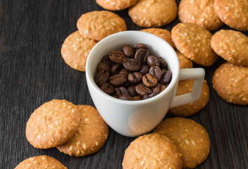white coffee Cup with coffee beans, sesame cookies on ebony background
