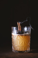 Glass of Scotch Whiskey orange juice alcohol cocktail with smoking cinnamon sticks
