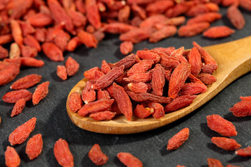 Extreme close up of dried organic goji berry fruits (wolfberries) in a wooden spoon on a black...