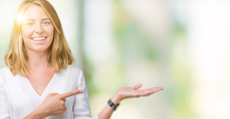 Beautiful young elegant woman over isolated background amazed and smiling to the camera while presenting with hand and pointing with finger.