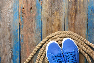Fototapeta na wymiar Blue sneakers shoes on a rope spiral, on a wooden weathered terrace. Yacht style concept. Template for avdertisement banner.