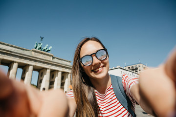 Young beautiful positive girl makes selfie against the background of the Brandenburg Gate in Berlin...