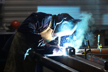 A man in a protective suit and mask welds pieces of iron