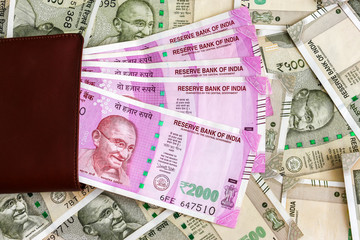 Close up view of leather wallet with brand new indian 2000 rupees banknotes. 500 rupee banknotes in background.