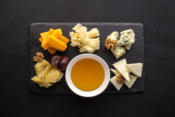 Many kinds of cheese with honey on stone plate on black background