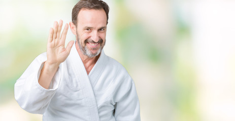 Naklejka premium Handsome middle age senior man wearing kimono uniform over isolated background Waiving saying hello happy and smiling, friendly welcome gesture