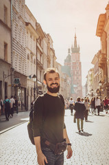 stylish bearded man with a tourist backpack behind his shoulder in the middle of an old street in the old European city of Krakow that is in Poland.