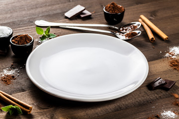 Empty white plate on dark wood, chocolate composition, angle view