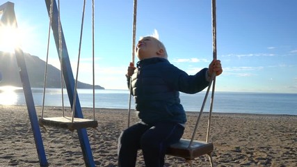 three year old boy swinging on a swing in the sunny morning on the beach