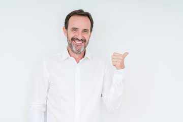 Elegant senior man over isolated background smiling with happy face looking and pointing to the side with thumb up.