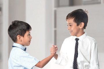 Two cheerful boys wearing  shirts and ties shake each other hands as a token of friendship