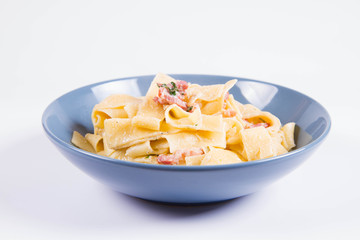 Pappardelle Carbonara on a blue plate on a white background