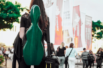 A girl holding a green cases for a musical instrument, for guitar, violin or double bass