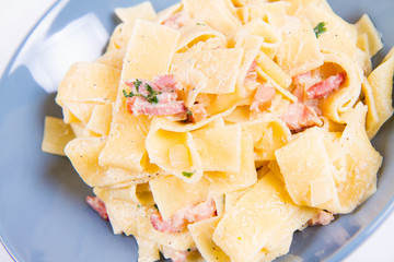 Pappardelle Carbonara on a blue plate on a white background