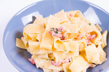 Pappardelle Carbonara on a blue plate on a white background
