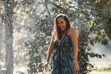 Girl being surprised by automatic watering and being wet in street or park. Girl in the rain having fun with cold water