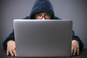 hacker in the hood in front of a laptop looks into the camera