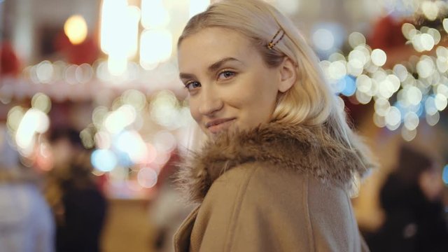 Portrait of young smiling woman at christmas market in a city. Happy attractive woman in a christmas market at night. Beautiful bokeh lights background.